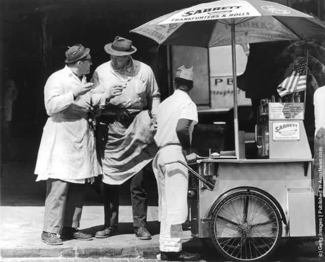 1965: Two butchers stop to chat after buying hot dogs from a street vendor in the Times Square area of New York