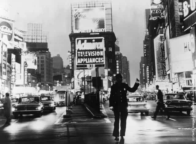 1965: A policeman directs traffic in front of the famous neon billboards of Times Square in New York City, at its intersection with Broadway