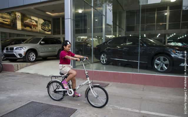 A Vietnamese girl rides her bicycle by a luxury car showroom