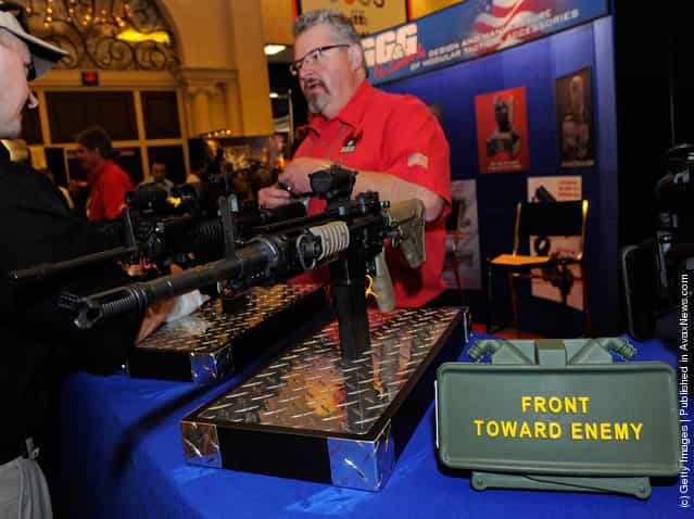 Brant Sabau with GG&G Inc. talks to attendees about the company's tactical rifle accessories behind an Airsoft AR-15 rifle and a replica claymore anti-personnel mine