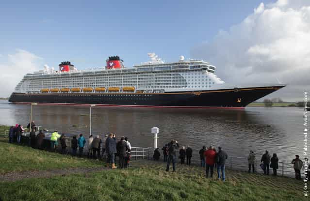 Tugboats haul the [Disney Fantasy] cruise ship backwards down Ems river after the ship departed from the Meyer Werft shipyards