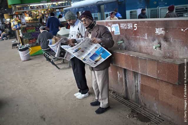 Men read newspapers as they wait for their train at the Nizamuddin Railway Station in New Delhi, India