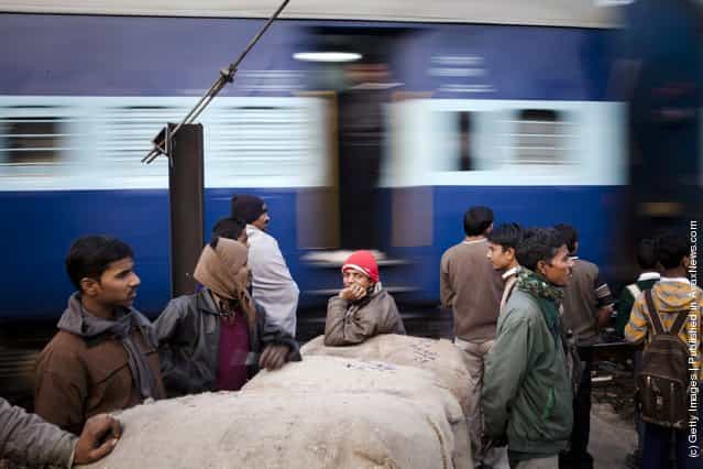 Workers wait to cross tracks as a train to passes nearby to the Nizamuddin Railway Station in New Delhi, India