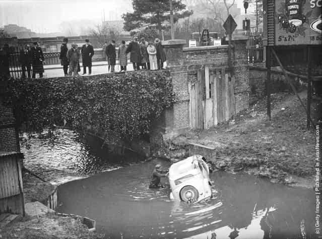 1936: A group of passers-by looking at a car which crashed through a fence and fell 20 feet into Wealdstone Brook, London