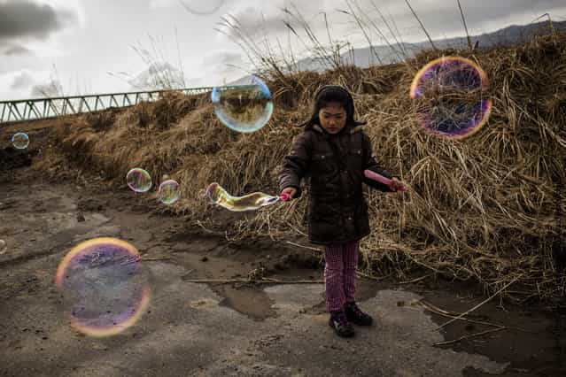 Hikari Oyama, 8, plays with bubbles, after she and her grandmother payed their respects at the memorial to victims of the last year's tsunami at the Okawa Elementary School, where 74 children were killed and 4 are still missing, on March 11, 2012 near Ishinomaki, Japan
