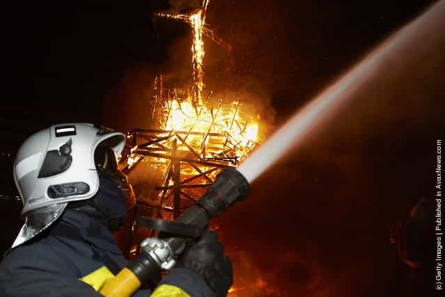 A fireman sprays water while a combustible Ninot caricature burns in the background during the last day of the Fallas festival on March 19, 2012 in Valencia, Spain
