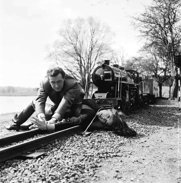 1965: Steed (played by Patrick MacNee) unties Emma Peel (Diana Rigg) as a miniature train comes down the track towards them in an episode of the TV series The Avengers