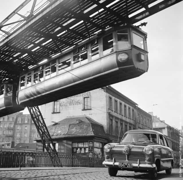 A hanging monorail train moves along the seven mile Wuppertal Monorail System in Germany, just over the path of the traffic, 1950