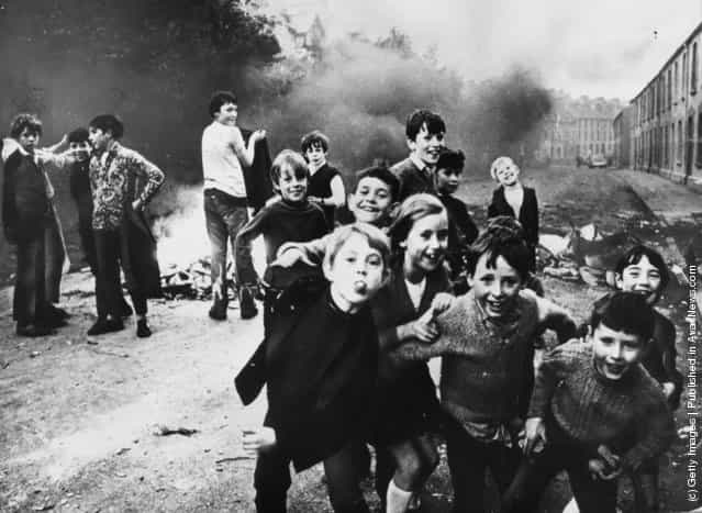 1971: Children jeer at British soldiers whiile a fire smoulders in the street behind them