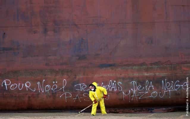 A French civil guard clears sand contaminated with fuel oil on Kerminihy beach after the TK Bremen cargo ship was stranded by high winds, on December 17, 2011. Graffiti on the side of the ship reads in French: [For Christmas, I wanted some snow, not fuel oil]