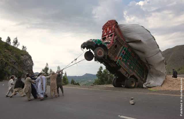 Men use ropes to try and right a supply truck overloaded with wheat straw along a road in Dargai, in the Malakand district, about 100 miles northwest of Pakistan's capital Islamabad, on April 13