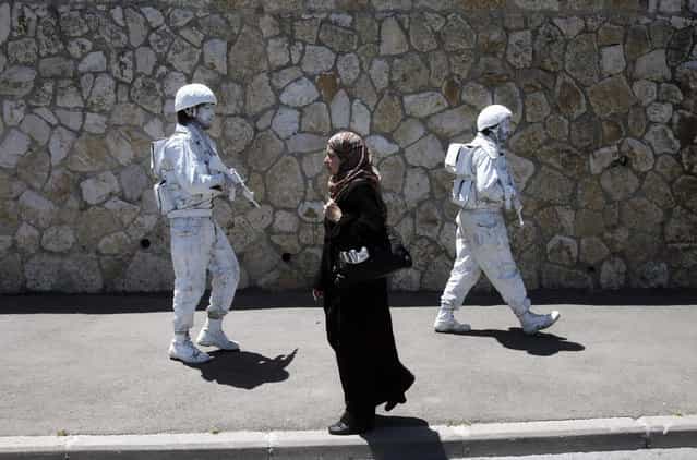 A woman walks past Israeli artists, one of them Yuda Braun (R), in Jerusalem. Braun says the [White Soldier], his artistic project launched in 2009, hopes to add to the discourse on the Israeli-Palestinian conflict
