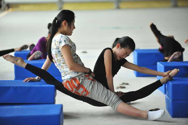 A coach sits on a student’s leg to help her stretch during a training session at a gymnastic course at Shenyang Sports School in Shenyang, Liaoning province
