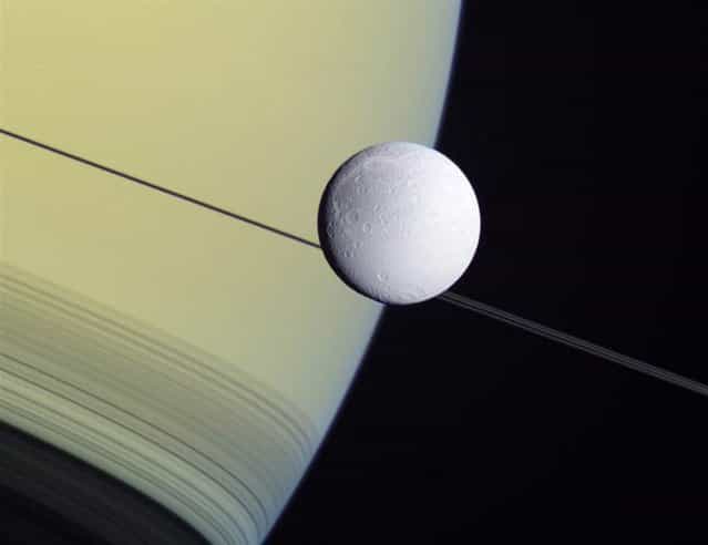 This wide-angle view from NASAs Cassini probe shows the Saturnian moon Dione set against the giant planets disk and rings on May 2 2012