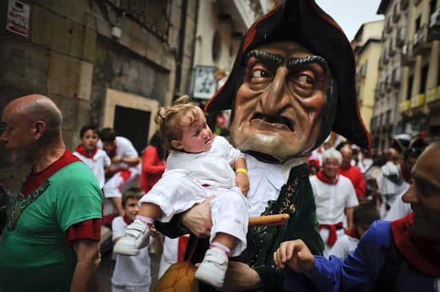 A man dressed as a giant holds a young girl during the giants and big heads parade of the San Fermin festival