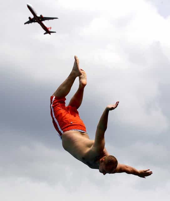 A man jumps from a tower into a public swimming pool while a plane takes off from the international airport in Duesseldorf, Germany