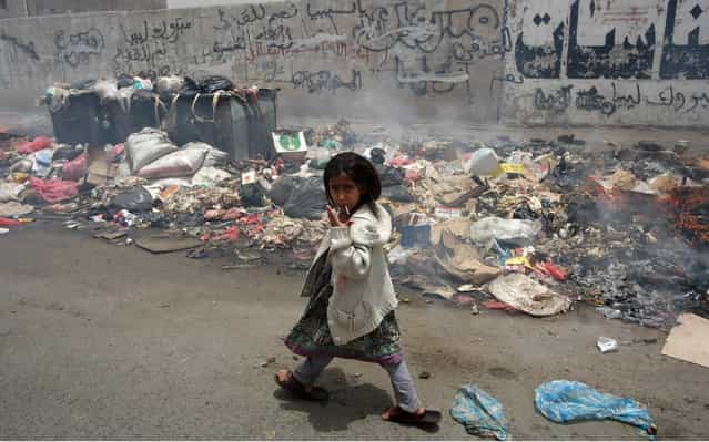 A Yemeni girl gestures while passing through a pile of garbage in the streets of Sanaa (Yemen), after garbage collectors completed their fifth day of strike in protest over pay on July 10, 2012