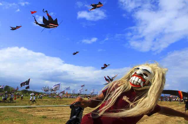 A boy wears a mask while flying a traditional kite during a kite festival on Padang Galak island of Bali, Indonesia