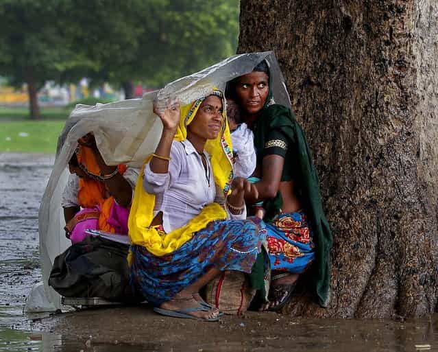 Women sit under a plastic sheet to shelter themselves from the rain in New Delhi, India on July 12, 2012