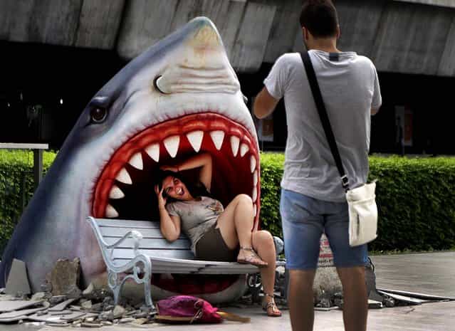 A tourist poses for a picture with a fake shark at a business district in Bangkok, Thailand on July 12, 2012