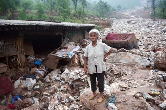 An elderly woman stands by her damaged home in the devasted area in Beijing on July 26, 2012, after the worst rainstorms in six decades pounded the capital city on July 21 leaving the metropolis flooded and tens of thousands of people stranded in surging waters. Authorities in Beijing said they would begin to "strike" out at online critics of the government response to recent record flooding, while declining again to release updated casualty tolls. (Photo by AFP)