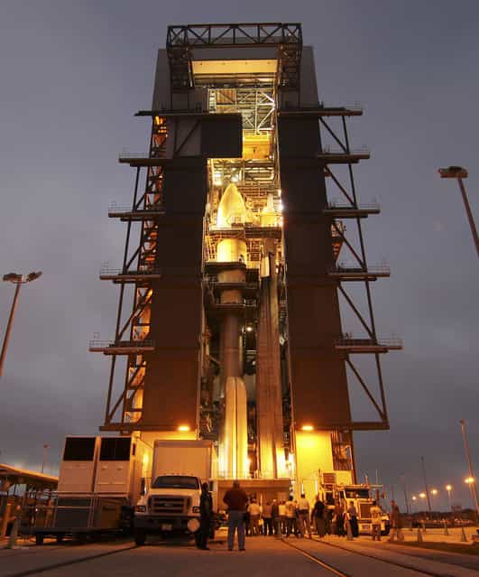 The Atlas V rocket set to launch NASAs Mars Science Laboratory mission is illuminated inside the Vertical Integration Facility at Space Launch Complex 41, where employees have gathered to hoist one of the final pieces to be integrated - the spacecrafts multi-mission radioisotope thermoelectric generator (MMRTG). The generator was lifted up to the top of the rocket and installed on the MSL spacecraft, encapsulated within the payload fairing. The MMRTG will generate the power needed for the mission from the natural decay of plutonium-238, a non-weapons-grade form of the radioisotope. (Photo by Dimitri Gerondidakis/NASA)