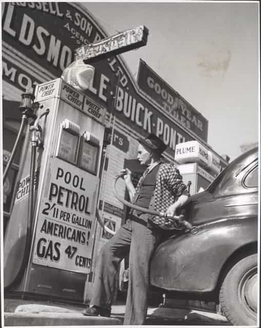 William Russell putting the four gallon monthly ration of petrol into a customers car, Drouin, Victoria, ca. 1944. Home town Australia. Drouins biggest service station (there are two) is owned by a company consisting of 80 year old William D. Russell and his family. Mr Russell is putting the four gallon monthly ration of gas onto a customers car
