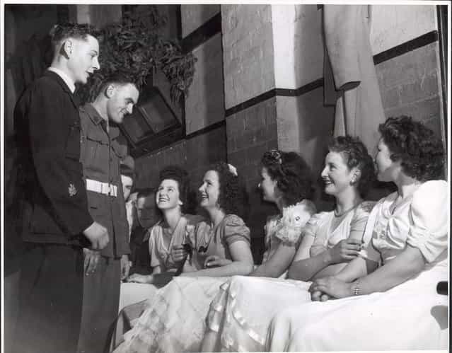 Wes Colquhoun and Fred Phair talking to the girls at the ball in the Soldiers Memorial Hall, Drouin, Victoria, ca. 1944. Pride of the stag line at Drouins weekly dance were bachelors – gay Warrant Officer Wes Colquhoun (23), R.A.A.F., and Corporal Fred Phair (25), A.I.F. Wes, son of Drouins butcher, was sole surviving member of a Lancaster Crew... Fred, son of Drouins fruiterer, served in New Guinea...