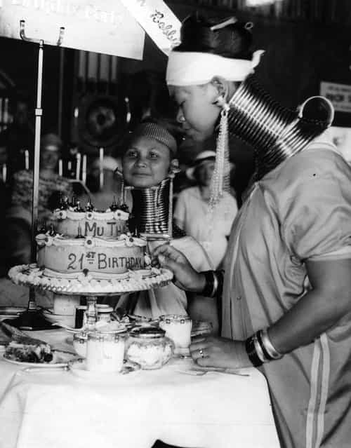 A Burmese woman, with traditional neck-extending rings, celebrates her twenty-first birthday with a cake in Folkestone with her friend. They are both part of Bertram Mills Circus, where they are billed as the [giraffe-necked Burmese ladies]. 25th August 1936. (Photo by A. J. O'Brien)