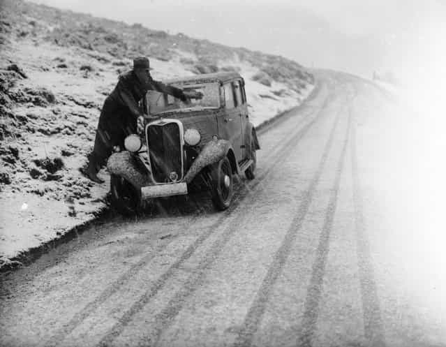 A driver on the Horseshoe Pass in North Wales wiping the snow from the windscreen of his car during a heavy snow storm, 18th January 1937. (Photo by Norman Smith)