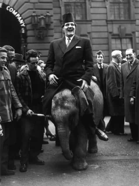Comic conjuror Tommy Cooper (1922–1984), wearing his trade-mark fez, riding Pioneer, a three year old elephant from Billy Smart's circus, to the opening of a joke and tricks shop in High Holborn. 23rd February 1959. (Photo by Keystone)