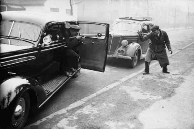 A [policeman] and a [gangster] shoot it out in the streets of London during a demonstration of a new eight-cyclinder saloon car with bulletproof windows and pivot holes for guns. The car is being tested by officials at the Criminal Investigation Department of Scotland Yard. 15th January 1937. (Photo by J. A. Hampton/Topical Press Agency)