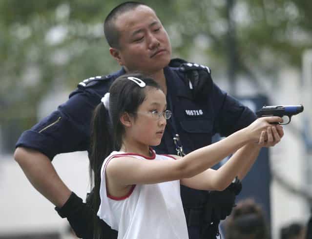 A young girl is taught how to aim a pistol by a police officer during the a Police Open Day at Shenzhen Police Training School on October 14, 2006 in Shenzhen, China. The event, displaying the latest equipment used by the police is held annually to improve the police's image and help to publicise security knowledge. (Photo by China Photos)