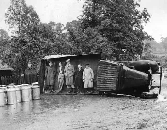 Passers-by use an overturned lorry as a shelter during a sudden shower of rain near Navestock, Romford, Essex. The lorry overturned on a sharp bend, discharging its load of milk churns, but the driver escaped uninjured. 15th June 1937. (Photo by Fox Photos)