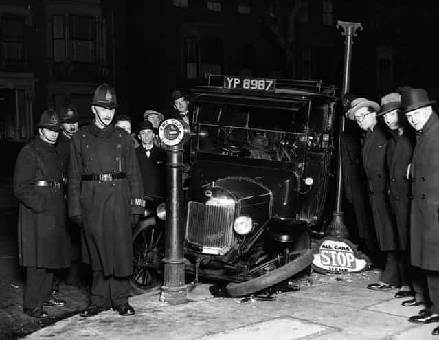 A group of policemen and passers-by survey the wreckage of a taxi in Stoke Newington, London. Its front wheel lies on the pavement next to a sign bearing the ironic instruction [All Cars Stop Here]. 14th February 1930. (Photo by Fox Photos)