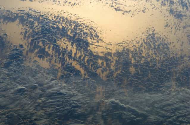 The setting sun highlights cloud patterns – as well as the Pacific Ocean surface itself – in this photograph taken by an astronaut aboard the International Space Station, on May 15, 2012. The ISS was located over the Andes Mountains of central Chile at the time. The camera view is looking back towards the Pacific Ocean as the Sun was setting in the west. (Photo by NASA)