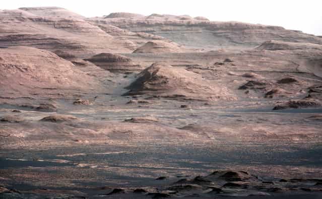This image is from a test series used to characterize the 100-millimeter Mast Camera on NASA's Curiosity rover. It was taken on August 23, 2012, and looks south-southwest from the rover's landing site. The 100-millimeter Mastcam has three times better resolution than Curiosity's 34-millimeter Mastcam, though it has a narrower field of view. In the distance, there are dark dunes and then the layered rock at the base of Mount Sharp. Some haze obscures the view, but the top ridge, depicted in this image, is 10 miles (16.2 kilometers) away. Scientists enhanced the color in this version to show the Martian scene under the lighting conditions we have on Earth, which helps in analyzing the terrain. (Photo by NASA/JPL-Caltech/MSSS)