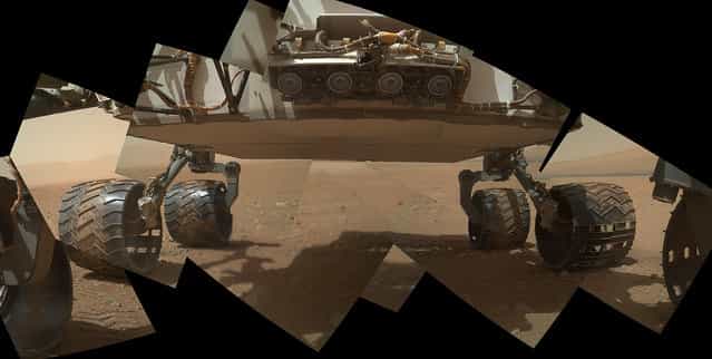 This view of the lower front and underbelly areas of NASA's Mars rover Curiosity combines nine images taken by the rover's Mars Hand Lens Imager (MAHLI) during the 34th Martian day, or sol, of Curiosity's work on Mars, on September 9, 2012. Curiosity's front Hazard-Avoidance cameras appear as a set of four blue eyes at the top center of the portrait. Fine-grain Martian dust can be seen adhering to the wheels, which are about 16 inches (40 centimeters) wide and 20 inches (50 centimeters) in diameter. The bottom of the rover is about 26 inches (66 centimeters) above the ground. On the horizon at the right is a portion of Mount Sharp, with dark dunes at its base. The camera is in the turret of tools at the end of Curiosity's robotic arm. (Photo by NASA/JPL-Caltech/Malin Space Science Systems)