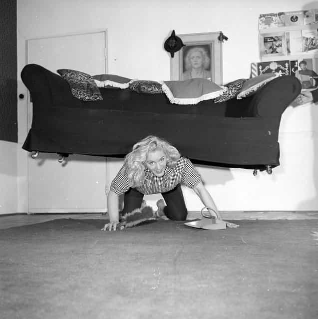 Glamorous strongwoman Joan Rhodes exercises her strength whilst tackling housework in her flat in Hampstead, north London, March 1958. (Photo by Ken Harding/BIPs)