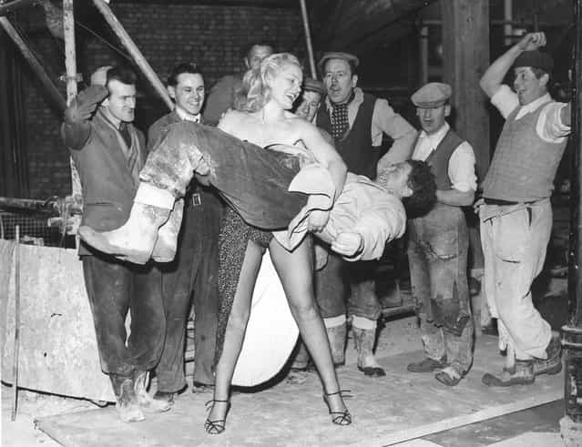 Men, working on the site of Quaglino's new banqueting rooms, look on in amazement as strong-woman Joan Rhodes demonstrates her strength by lifts one of their co-workers. She is appearing in cabaret at Quaglino's restaurant and decided to visit the men working next door. 8th April 1958. (Photo by Reg Speller/Fox Photos)