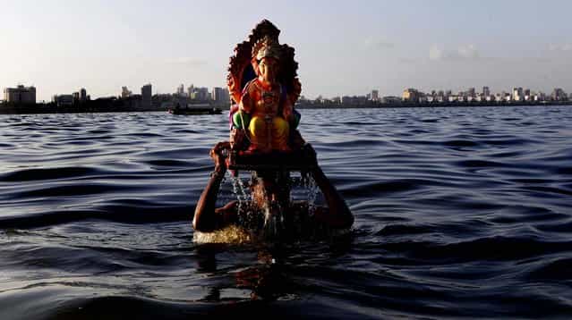A man carries an idol of the Hindu elephant-headed god Ganesha to immerse it in the Arabian Sea on the fifth day of the ten day long Ganesh Chaturthi festival in Mumbai, India, on September 25, 2012. (Photo by Rajanish Kakade/Associated Press)