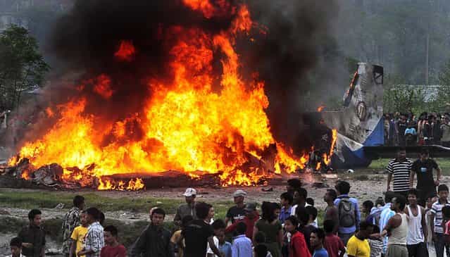 People gather around the burning wreckage of a Sita Air plane near Katmandu, Nepal, on September 28, 2012. The plane carrying trekkers to the Everest region crashed and burned just after takeoff in Nepal's capital, killing the 19 Nepali, British and Chinese people on board, authorities said. (Photo by Associated Press)