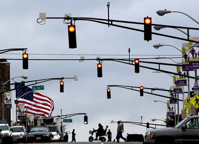 A flag waves in gusty winds as pedestrians cross the street in Newark, New Jersey, on September 18, 2012. A tornado watch was issued for parts of New Jersey, New York City and New York's lower Hudson Valley. (Photo by Julio Cortez/Associated Press)