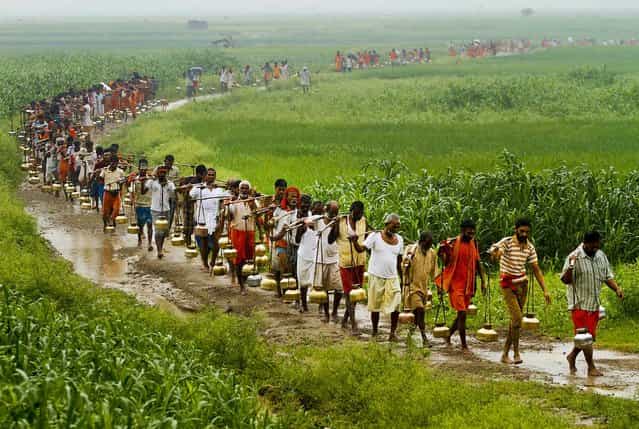 Hindus carrying metal pots filled with water from the River Ganges, walk to a Lord Shiva temple to perform a ritual during [Malmas] in Allahabad, India, on September 16, 2012. [Malmas] is an extra lunar month according to the Hindu calendar that occurs once in three years and is considered auspicious for Shiva worship. (Photo by Rajesh Kumar Singh/Associated Press)