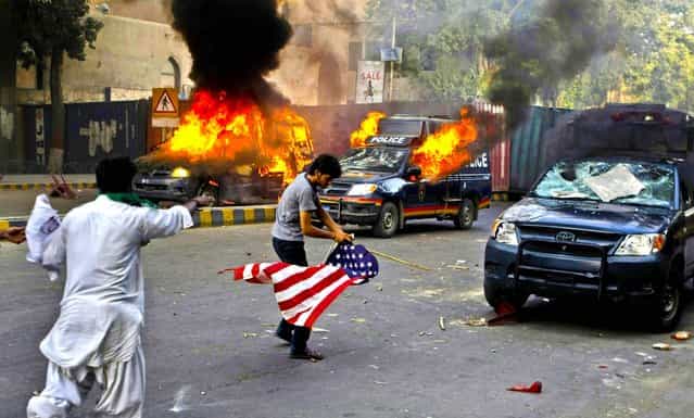 A protester carries a flag as police vehicles burn in Karachi, Pakistan, on September 21, 2012. Tens of thousands protested against the film around the country after the government encouraged peaceful protests and declared a national holiday [Love for the Prophet Day]. Demonstrations turned violent and scores of people were killed died after police opened fire on rioters torching a cinema in the northwest city of Peshawar. (Photo by Fareed Khan/Associated Press)