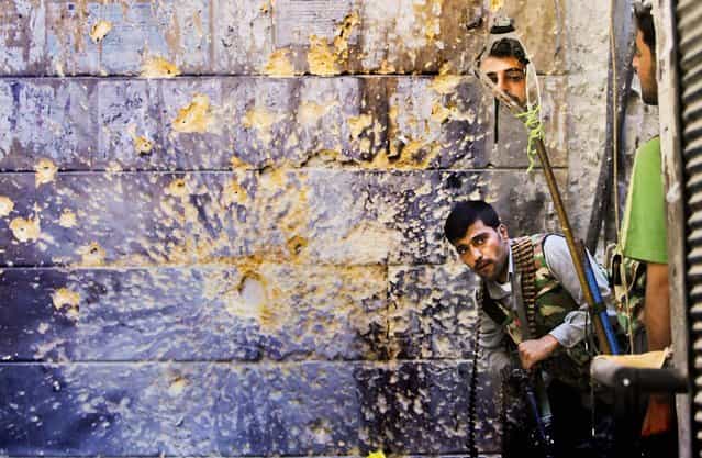 A Free Syrian Army soldier looks through a mirror which helps him see Syrian troops from the other side, as he takes his position with his comrade during fighting, at the old city of Aleppo city, Syria, on September 24, 2012. (Photo by Hussein Malla/Associated Press)