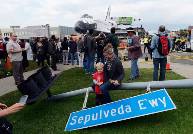 One of hundreds of street signs temporarily removed for the 12-mile road trip of space shuttle Endeavour is used as prop as a family gets their picture taken with the orbiter parked in a mall parking lot in Los Angeles, California. (Photo by Kevork Djansezian)