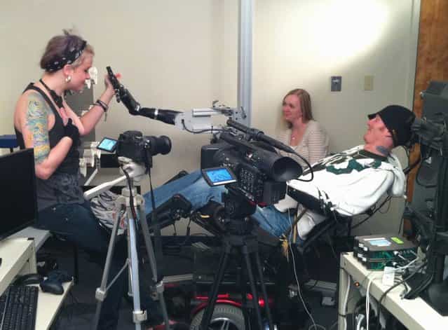 This handout frame grab from video, provided by the University of Pittsburgh Medical Center (UPMC), taken Monday, September 19, 2011, shows quadriplegic research subject Tim Hemmes operating a mechanical prosthetic arm with Katie Schaffer during a testing sessions at a UPMC research facility in Pittsburgh. Hemmes had a chip implanted on the surface of his brain that reads his intention to move his paralyzed arm and sends that instruction instead to an advanced bionic arm. The goal is to create mind-controlled prosthetics to restore some independence to the paralyzed. (Photo by AP Photo/UPMC)