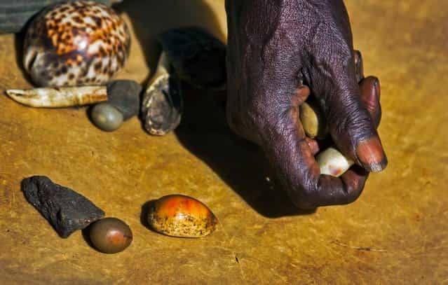 Kenyan witch-doctor John Dimo, who claims to be 105 years old, throws shells, bones, and other magic items to predict the outcome of the presidential election, in front of his hut in the village of Kogelo, where President Barack Obama's late father came from and whom Dimo claims to have known, in western Kenya, November 5, 2012. He said Obama will win. (Photo by Ben Curtis/Associated Press)