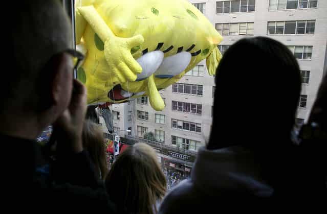 Spectators look at the Sponge Bob Square Pants balloon through a window on 6th Avenue during the 86th annual Macy's Thanksgiving Day Parade in New York. (Photo by Steve Berman/The New York Times)